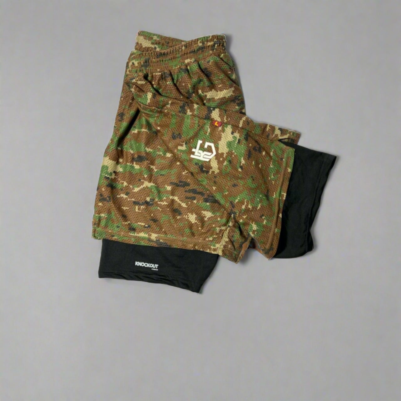 Elevate your workouts with Knockout Double Layer Camo Shorts – durable, moisture-wicking, and stylish with woodland camo and navy blue mesh layers.