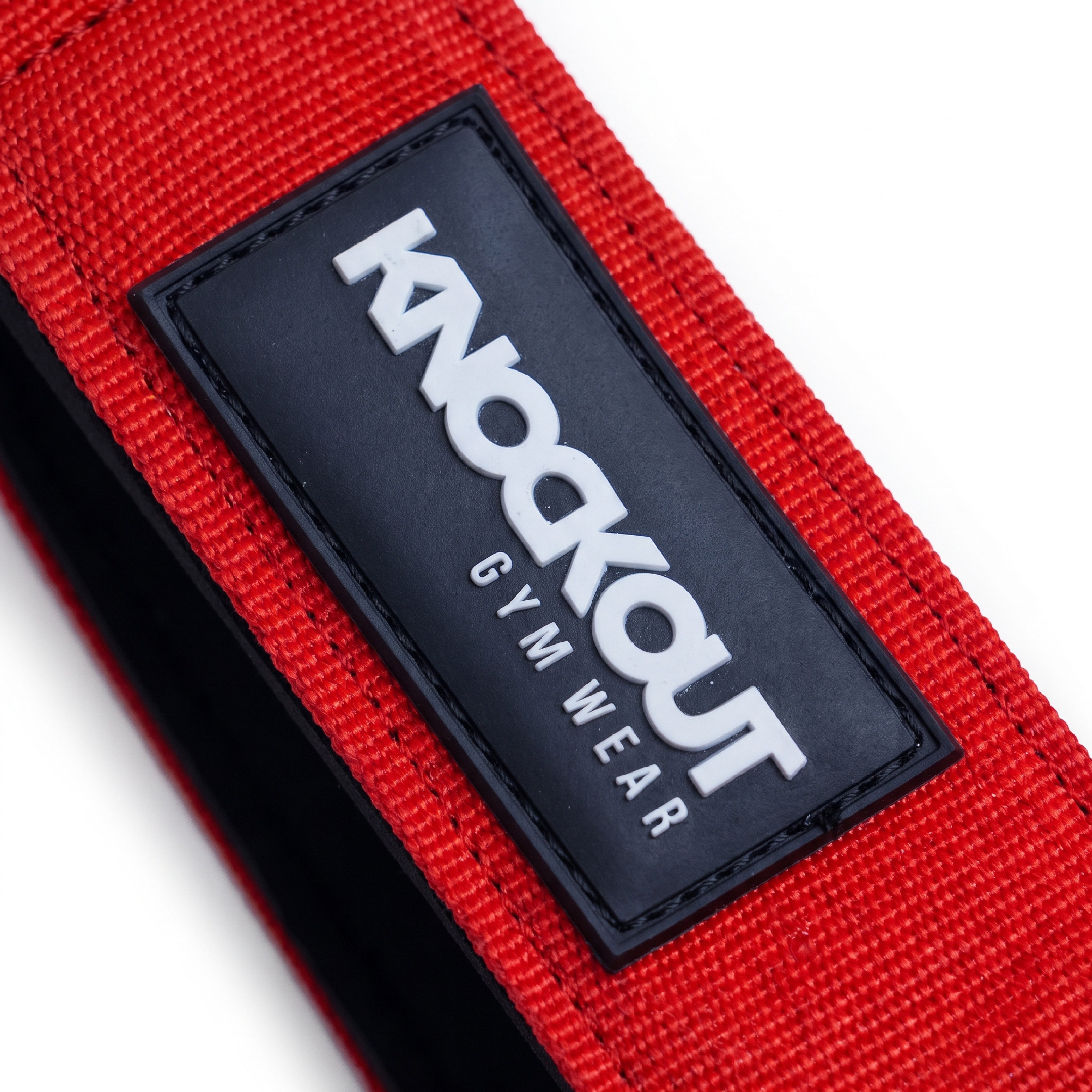 Close-up of a red gym belt with a black rectangular patch featuring the white text 'KNOCKOUT GYM WEAR'.